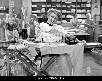 États-Unis : c. 1930. Une femme souriante reporte ses vêtements avec un fer à repasser dans une blanchisserie. Banque D'Images