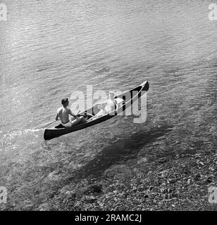 Parc national Jasper, Alberta, Canada : c. 1960 Une famille pagague un canot sur le lac Beauvert transparent, devant le Jasper Park Lodge, dans les Rocheuses canadiennes. Banque D'Images