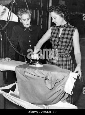 États-Unis : c. 1935. Une jeune femme fer une chemise tandis qu'une femme plus âgée se tient près et lui donne des instructions. Banque D'Images