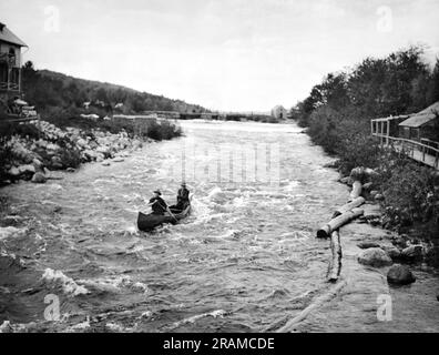 Grand Lake Stream, Maine : c. 1917 deux hommes dans un canot tirant sur les rapides de Grand Lake Stream. Banque D'Images