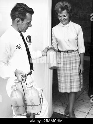 Californie: c. 1955 Un milkman de lait Sun Valley Dairy livrant du lait et de la limonade en bouteilles de verre à une maison où il est accueilli à la porte par la femme au foyer. Banque D'Images