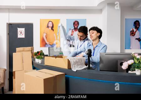 Équipe de magasin diversifiée travaillant aux commandes en ligne, mettant des vêtements à la mode dans des boîtes en carton dans le centre commercial. Les employés de la boutique préparent les colis pour la livraison, discutent de l'expédition detalis Banque D'Images