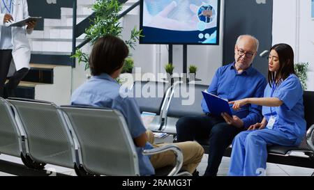 Infirmière expliquant le traitement de santé à un patient âgé lors de la consultation de visite de contrôle en salle d'attente à l'hôpital. Homme senior tenant une presse-papiers remplissant le rapport d'assurance médicale. Concept de médecine Banque D'Images