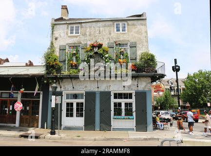 Scène de rue dans le quartier français. Les gens se mêlent près d'un ancien bâtiment avec des volets et un balcon en fer forgé richement décoré avec des fleurs. Banque D'Images