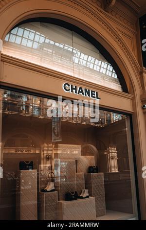 L'entrée de la boutique Chanel est chic et esthétique. Support beige neutre avec sac à main noir et chaussures blanches dans la fenêtre d'un magasin de luxe. Marque haute couture Banque D'Images