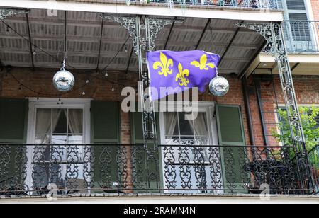 Balcon festif sur une vieille maison en briques dans le quartier français avec de grandes boules d'argent et un drapeau fleur de lis violet. Banque D'Images