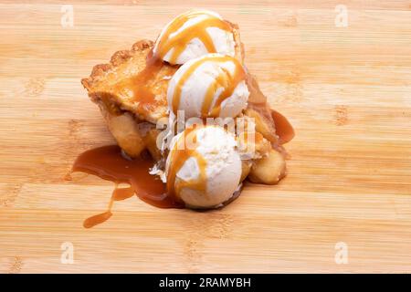 Une tranche de grosse tarte aux pommes avec un filet de caramel et trois boules de crème glacée à la gousse de vanille. Banque D'Images