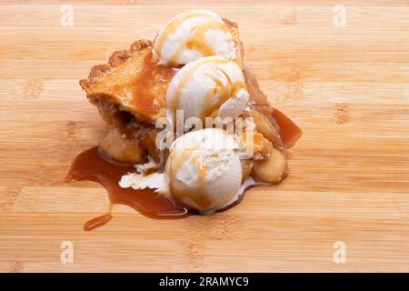 Une grosse tranche de tarte aux pommes arrosée de caramel et de trois boules de glace à la gousse de vanille fondant lentement. Banque D'Images