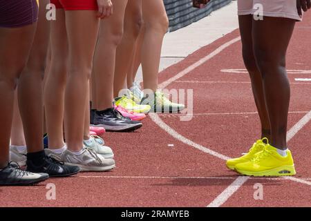 Les coureurs d'athlétisme et l'entraîneur se sont alignés avant la course sur la piste, montrant uniquement les jambes et les crampons. Banque D'Images