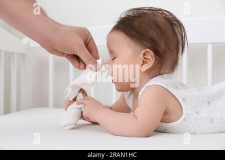 Père essuyant le nez liquide du petit bébé avec une serviette sur le lit, gros plan Banque D'Images