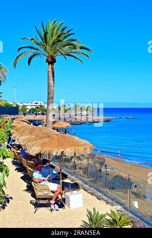 Lanzarote Îles Canaries Puerta del Carmen plage principale et palmiers et parasols en paille avec ciel bleu profond et mer Banque D'Images