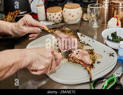 Le chef coupe des côtes d'agneau avec de la sauce à l'ail et à la moutarde, après cuisson au four Banque D'Images