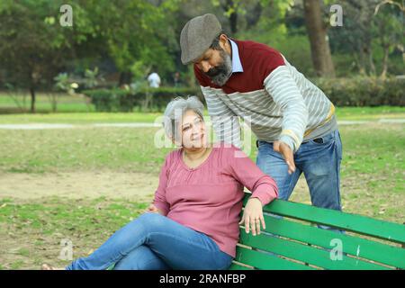 Couple de vieillesse assis sur le banc dans un environnement verdoyant et serein ayant un bon moment ensemble. Ils profitent joyeusement de leur temps. Banque D'Images