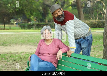 Couple de vieillesse assis sur le banc dans un environnement verdoyant et serein ayant un bon moment ensemble. Ils profitent joyeusement de leur temps. Banque D'Images