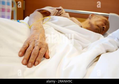 Main de patient âgé avec goutte intraveineuse au lit d'hôpital Banque D'Images