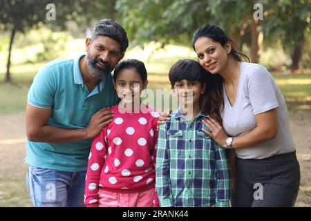 Famille indienne heureuse de père, mère, fils et une fille s'amusant dans le parc vert dans une journée dans un environnement vert et frais. Banque D'Images