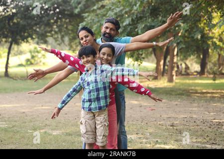 Famille indienne heureuse de père, mère, fils et une fille s'amusant dans le parc vert dans une journée dans un environnement vert et frais. Banque D'Images