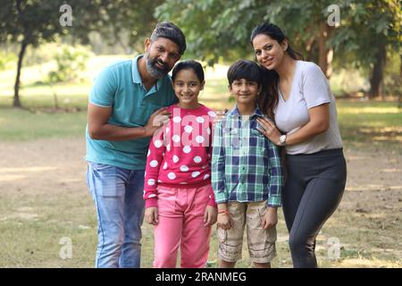 Famille indienne heureuse de père, mère, fils et une fille s'amusant dans le parc vert dans une journée dans un environnement vert et frais. Banque D'Images