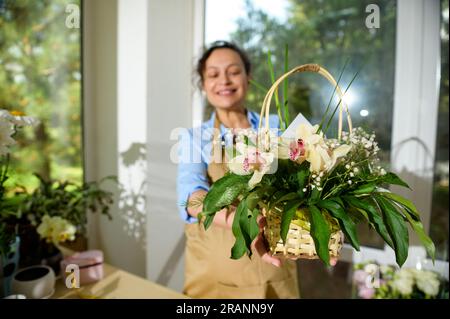 Beau bouquet de fleurs d'orchidées disposées dans un panier en osier, dans les mains d'un fleuriste souriant flou, pour l'événement de la vie festive. Arrangement floral WIT Banque D'Images