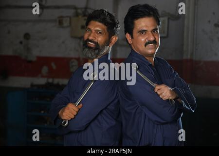 Portrait de mécaniciens automobiles indiens heureux debout ensemble dans la station-service. Spécialistes de voiture tenant des outils de réparation de voiture. Réparateurs professionnels Banque D'Images