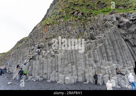 Plage de sable noir de Reynisfjara, Islande - 06.22.2023 : personnes grimpant sur des colonnes de basalte sur la plage de Reynisfjara Banque D'Images