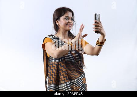 Femme heureuse indienne rurale à Saree prenant selfie et faisant un appel vidéo dans un village. Elle tient un téléphone portable pour le concept de digitalisation Banque D'Images