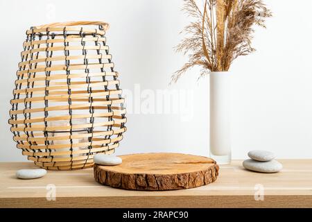 Décor minimal en bois naturel avec socle en disque en pin avec écorce, roseau sec dans un vase et lanterne ronde en bois avec bougie, mur blanc. Banque D'Images