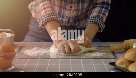 Pain artisanal travaillant avec de la pâte. Pétrissage à la main du pain dans la cuisine avec des outils d'équipement de boulangerie au premier plan et fond noir. Panification Banque D'Images