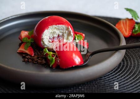 Mise au point sélective d'un gâteau caillé sphérique avec sauce fraise sur une assiette noire. Morceau de gâteau sur la cuillère noire. Fraises et brownies. Dessert rouge. Banque D'Images