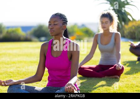 Groupe d'amis divers faisant du yoga et méditant dans le jardin. Amitié, mode de vie sain et actif, été, soleil, inaltéré. Banque D'Images