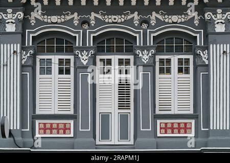 Shophouse traditionnel chinois Peranakan de détroit avec extérieur gris et volets en bois blanc persiennes, carreaux floraux et colonnes de plâtre ornées Banque D'Images