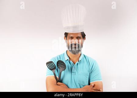Portrait d'un chef barbu indien portant un t-shirt et une casquette de chef. Heureux souriant expressions fond blanc. Tenir la spatule et la cuillère à frire dans la main Banque D'Images