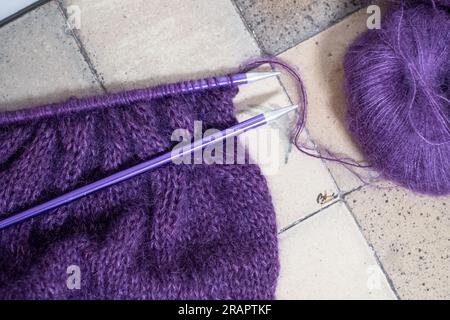 Gros plan de pull tricoté à la main en mohair violet et en fil d'alpaga avec des mailles, y compris le point de bas et la côte, tricoté sur des aiguilles à tricoter droites. Banque D'Images