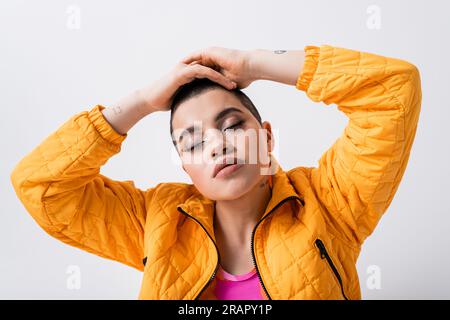 déclaration de mode, jeune femme tatouée dans des vêtements colorés assis les yeux fermés sur fond gris, style urbain, individualisme, dynamique et jeunesse Banque D'Images