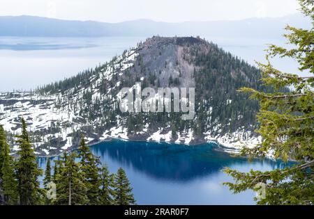 Vue sur Wizard Island dans les eaux bleues profondes de la Caldera au lac Crater par un jour brumeux Banque D'Images