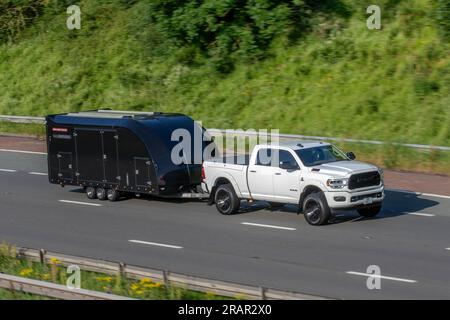 Brian James Race transporter 6 - remorque de voiture noire fermée, remorque de voiture à trois essieux remorquée par 2019 DODGE RAM USA voyageant à grande vitesse sur l'autoroute M6 dans le Grand Manchester, Royaume-Uni Banque D'Images