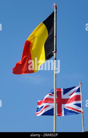 Au premier plan, le drapeau belge et en arrière-plan, le drapeau anglais agitant dans un ciel dégagé. Banque D'Images