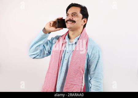 Portrait d'un homme fermier barbu indien heureux dans le concept de l'Inde rurale. Fond blanc des expressions funky. Fermier joyeux parlant sur un téléphone portable Banque D'Images