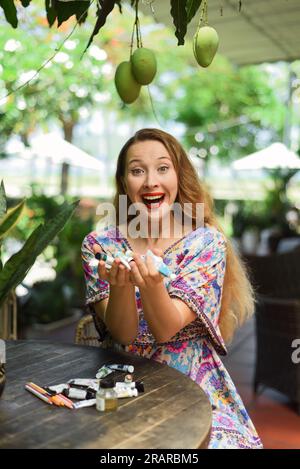 Portrait de belle femme blonde artiste et illustrateur assis à la table et tenant heureusement ses peintures acryliques Banque D'Images