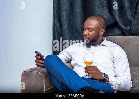 Homme d'affaires se détend sur un canapé tenant un verre de vin et utilisant un smartphone pour la communication Banque D'Images