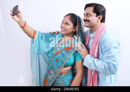 Couple de village indien rural prenant heureux un selfie à partir d'un téléphone portable. Femme portant Saree et homme en kurta. Banque D'Images