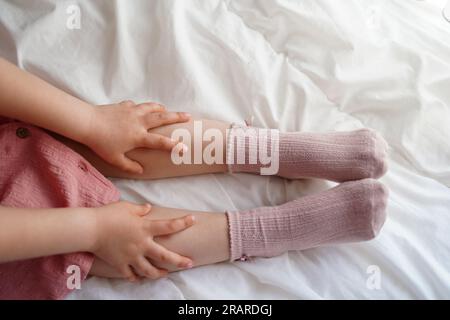 Jambes de fille de l'enfant en chaussettes roses avec les mains sur un lit dans une maison confortable Banque D'Images