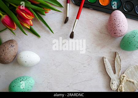 Oeufs faits à la main peints de pâques multicolores, tulipes rouges, peintures et pinceaux. Cadre festif de Pâques sur fond blanc avec espace de copie pour le texte Banque D'Images