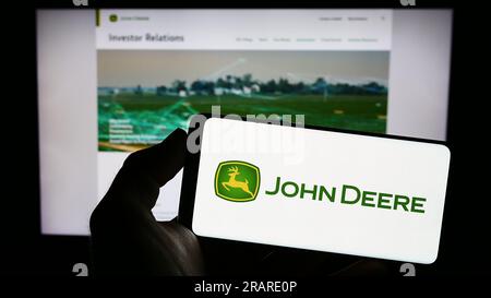 Personne tenant le smartphone avec le logo de la société américaine Deere and Company (John Deere) sur l'écran devant le site Web. Concentrez-vous sur l'affichage du téléphone. Banque D'Images