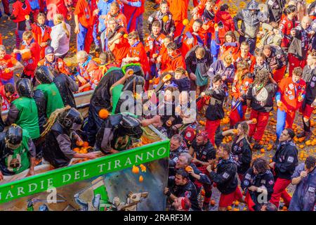 Ivrea, Italy - February 19, 2023: Groups in traditional dressings, and crowd with red hats, take part in the Battle of the Oranges, part of the histor Banque D'Images