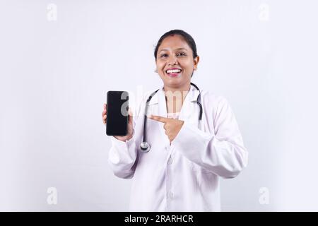 Beau portrait d'un docteur indien heureux en uniforme portant stéthoscope montrant l'écran du téléphone en main. Banque D'Images