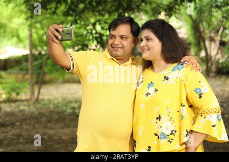 Heureux Jeune beau couple indien debout sur le sentier ensemble, prenant selfie avec leur téléphone portable. Banque D'Images
