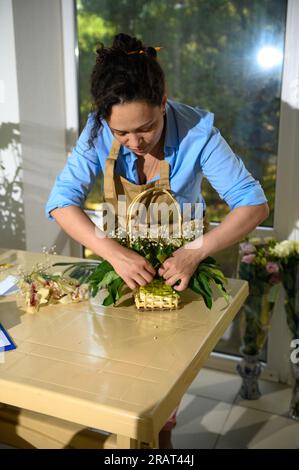 Belle femme portant un tablier beige, entrepreneur fleuriste inspiré travaillant sur l'arrangement floral dans le studio de design floral. Floristique. Boutique de fleurs. ARR Banque D'Images