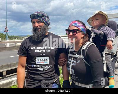 Chris Lewis, Kate Barron et leur fils Magnus au pont Severn à Chepstow. M. Lewis, ancien parachutiste britannique qui parcourt le littoral britannique depuis six ans, est retourné dans son pays natal, le pays de Galles, pour la première fois depuis son départ. M. Lewis, 43 ans, a parcouru 19 000 km depuis qu’il a quitté la plage de Llangennith sur la péninsule de Gower, près de sa ville natale de Swansea, au sud du pays de Galles, en août 2017. Date de la photo : mercredi 5 juillet 2023. Banque D'Images