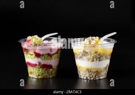 Gâteaux à emporter dans des verres avec pistaches, mousse de fraise, biscuit aux graines de pavot et caillé de citron sur fond noir Banque D'Images